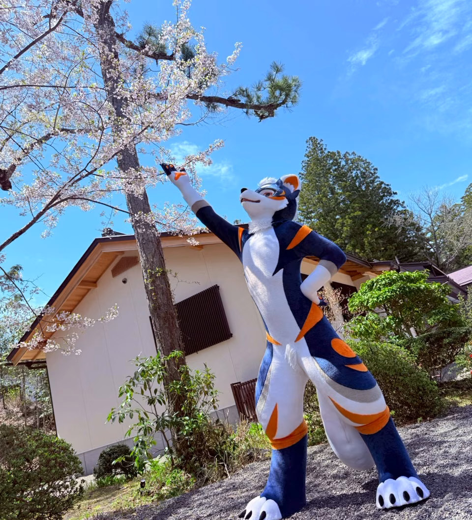 Blue NEOERA character beside spring blossoms